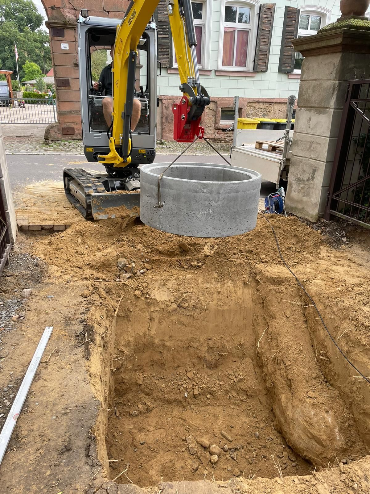 Referenzbild: Ein gelber Bagger hebt einen Betonring in den Boden.