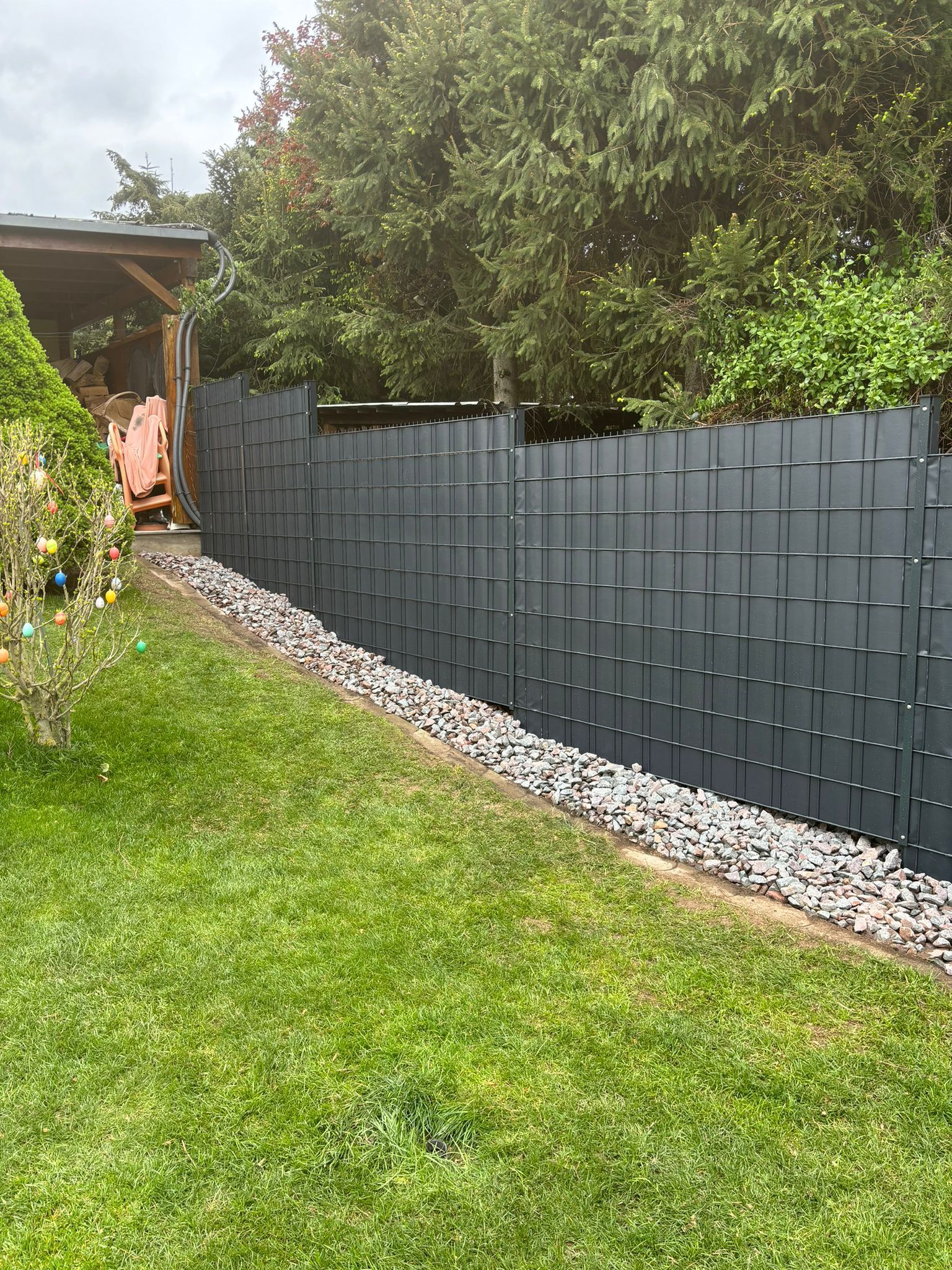 Referenzbild:In der Mitte eines üppig grünen Hofes steht ein schwarzer Zaun.