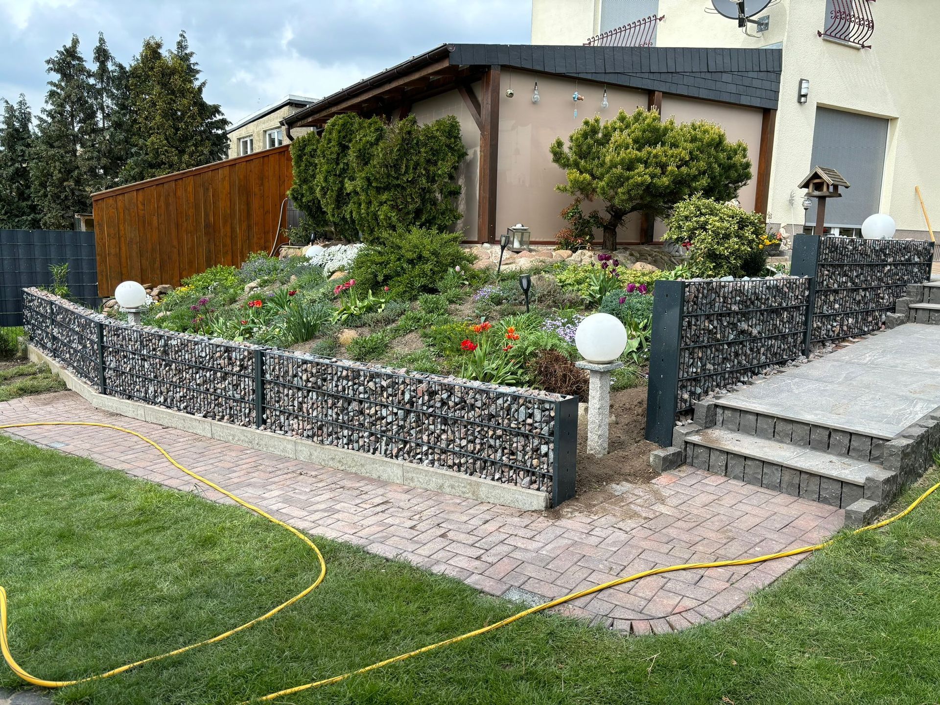 Referenzbild: Ein Garten mit einer Steinmauer und einer Treppe vor einem Haus.