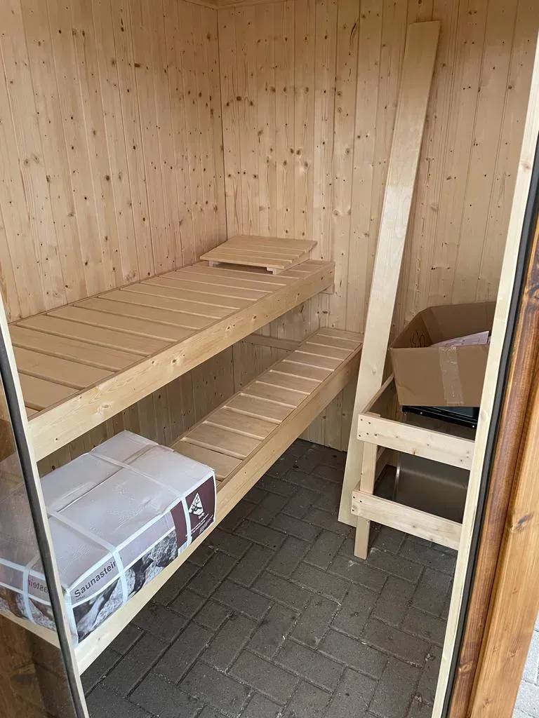 Referenzbild: Innenansicht der kleinen Sauna aus dunklem Holz unter einem erweiterten Carport