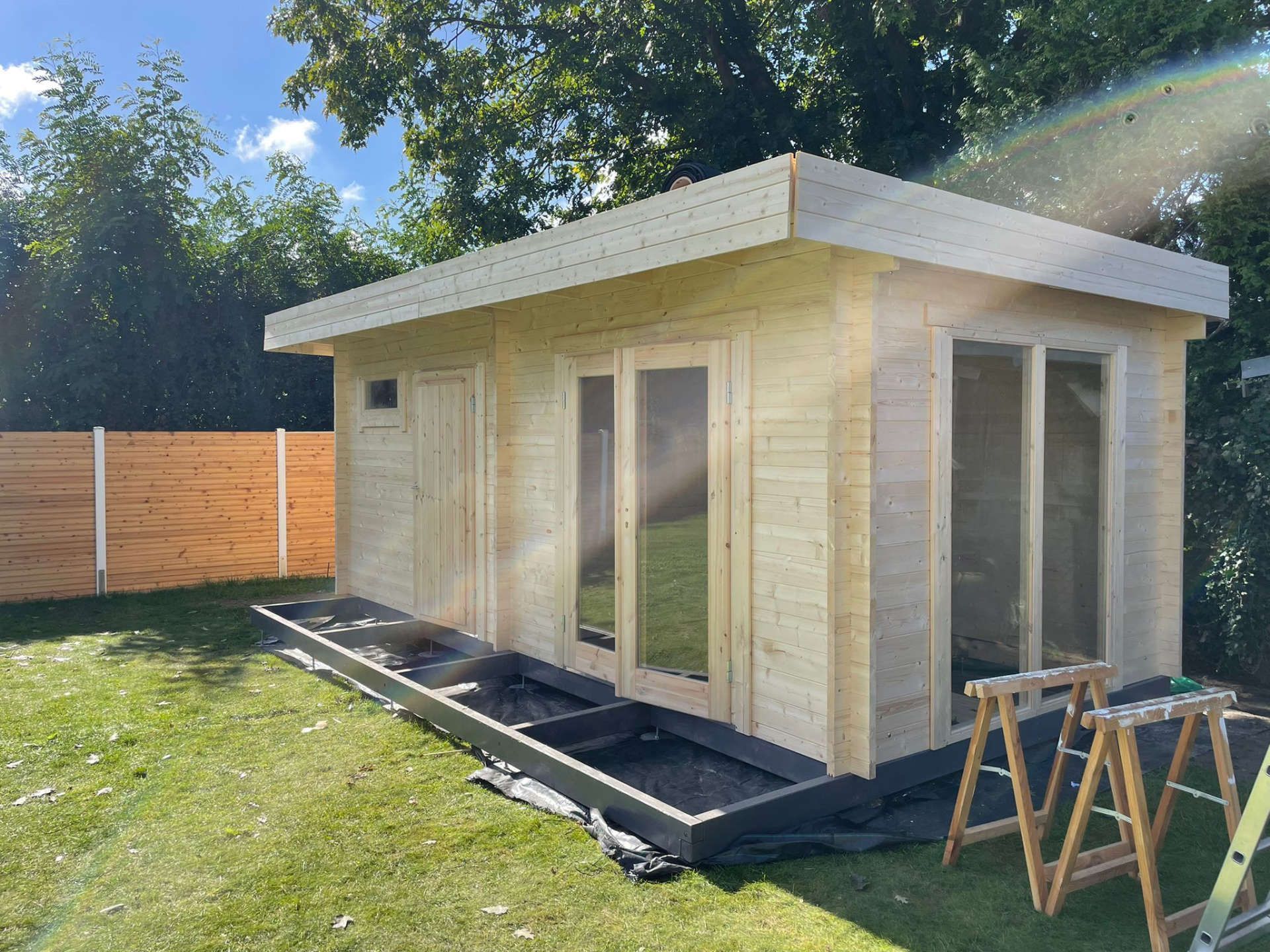 Referenzbild: Gartenhaus mit Terrassenanbau aus sehr hellem Holz sowie ebenerdigen Fenstern und Türen