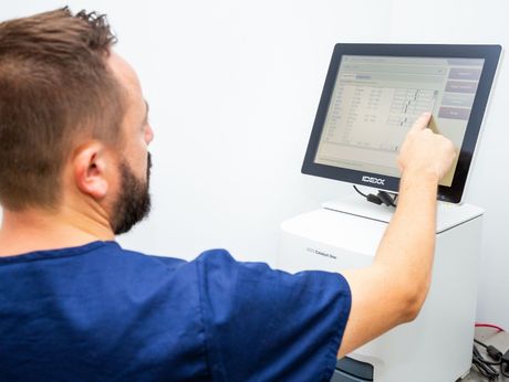 Un hombre con un uniforme azul señala una pantalla de computadora.