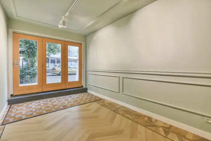 Pasillo amplio y luminoso con suelo de madera en espiga, paredes blancas y puertas francesas de cristal al final.