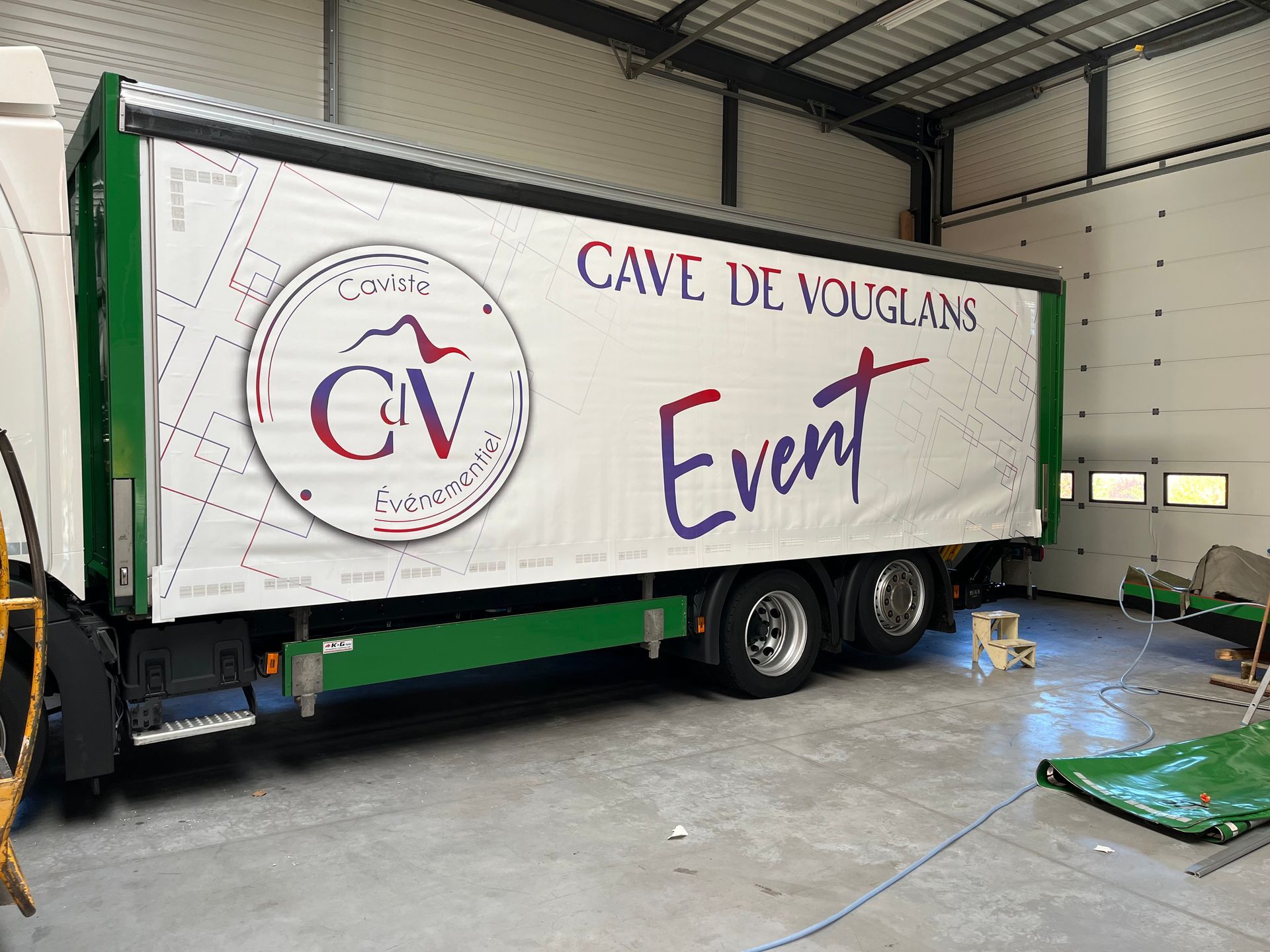 Camion blanc avec le logo « Événement Cave de Vouglans » sur le côté, stationné dans un garage.