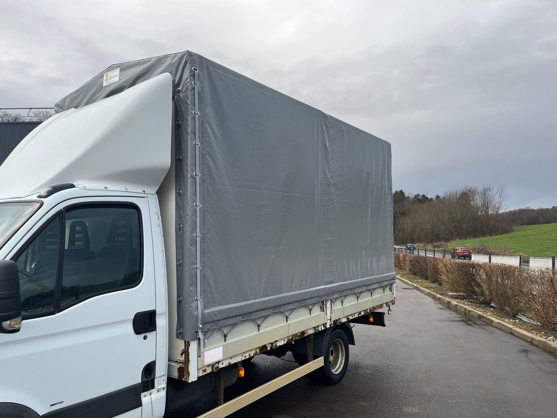 Un camion blanc, dont la benne est recouverte d'une bâche grise