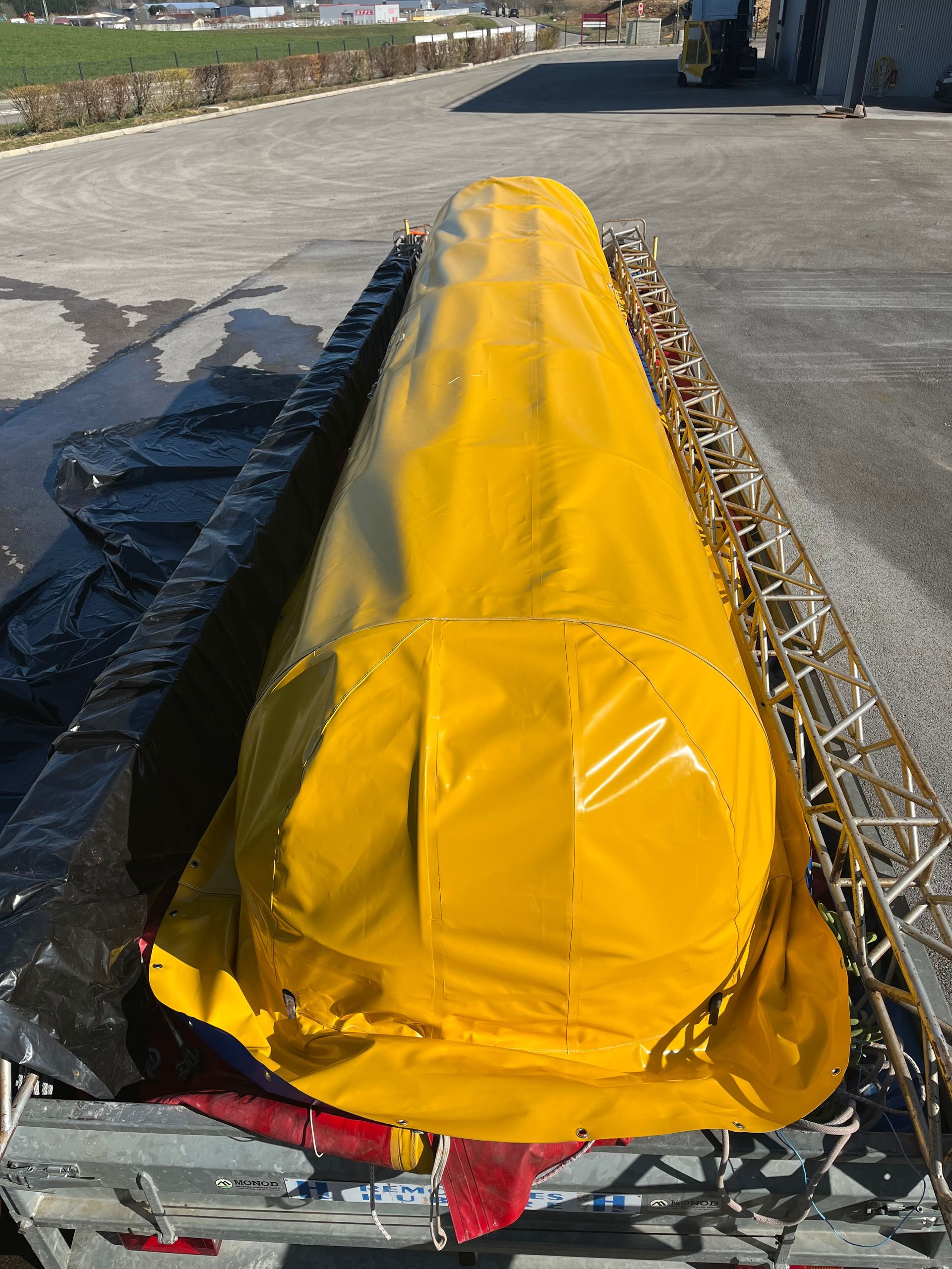 Objet cylindrique recouvert d'une bâche jaune sur un camion plateau, probablement du matériel.