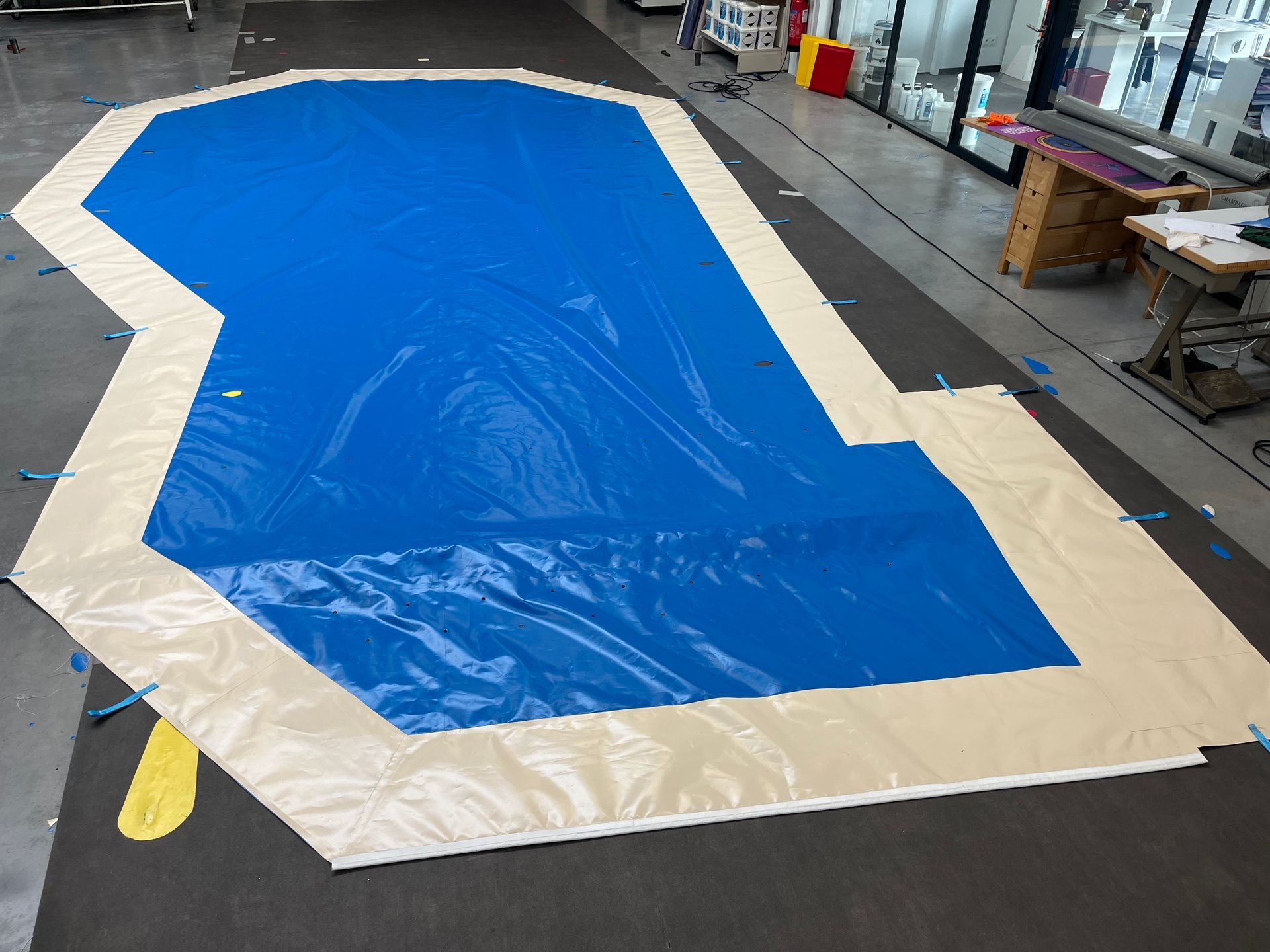 Grande bâche bleue et beige sur le sol d'un atelier, découpée pour servir de piscine.