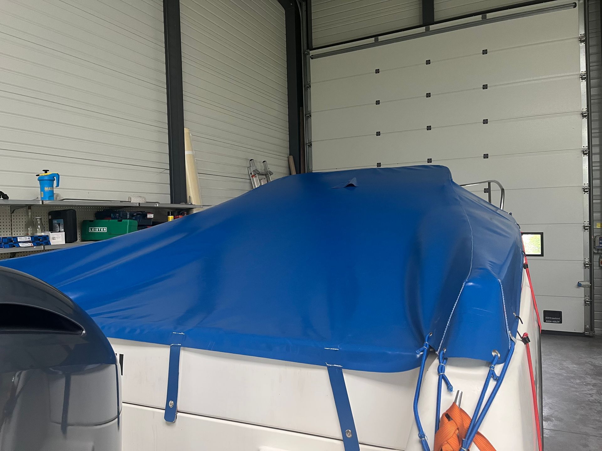 Une bâche bleue recouvre un bateau blanc à l'intérieur d'un garage.