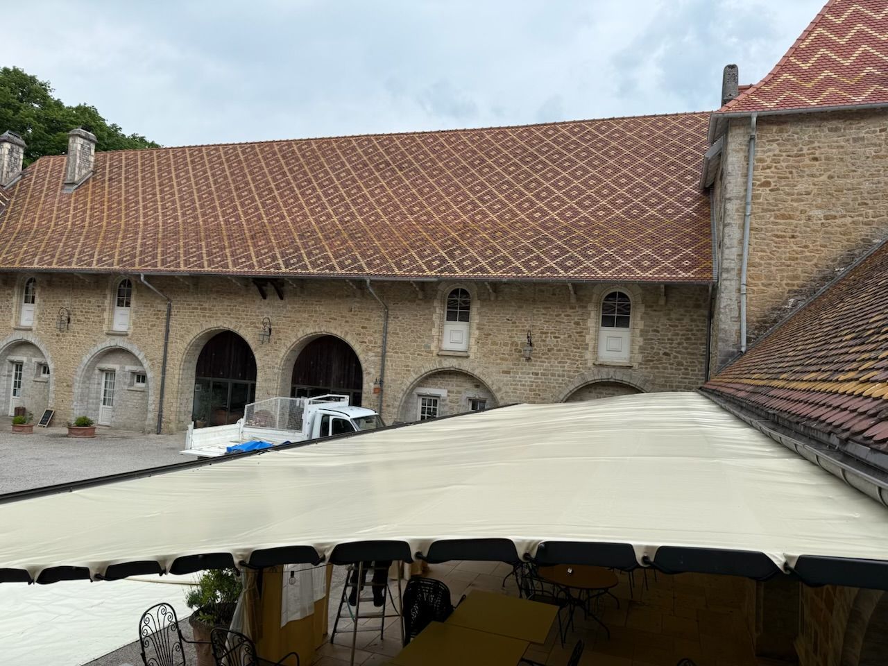Vue extérieure d'un bâtiment en pierre avec un toit de tuiles rouges, avec un auvent au premier plan.