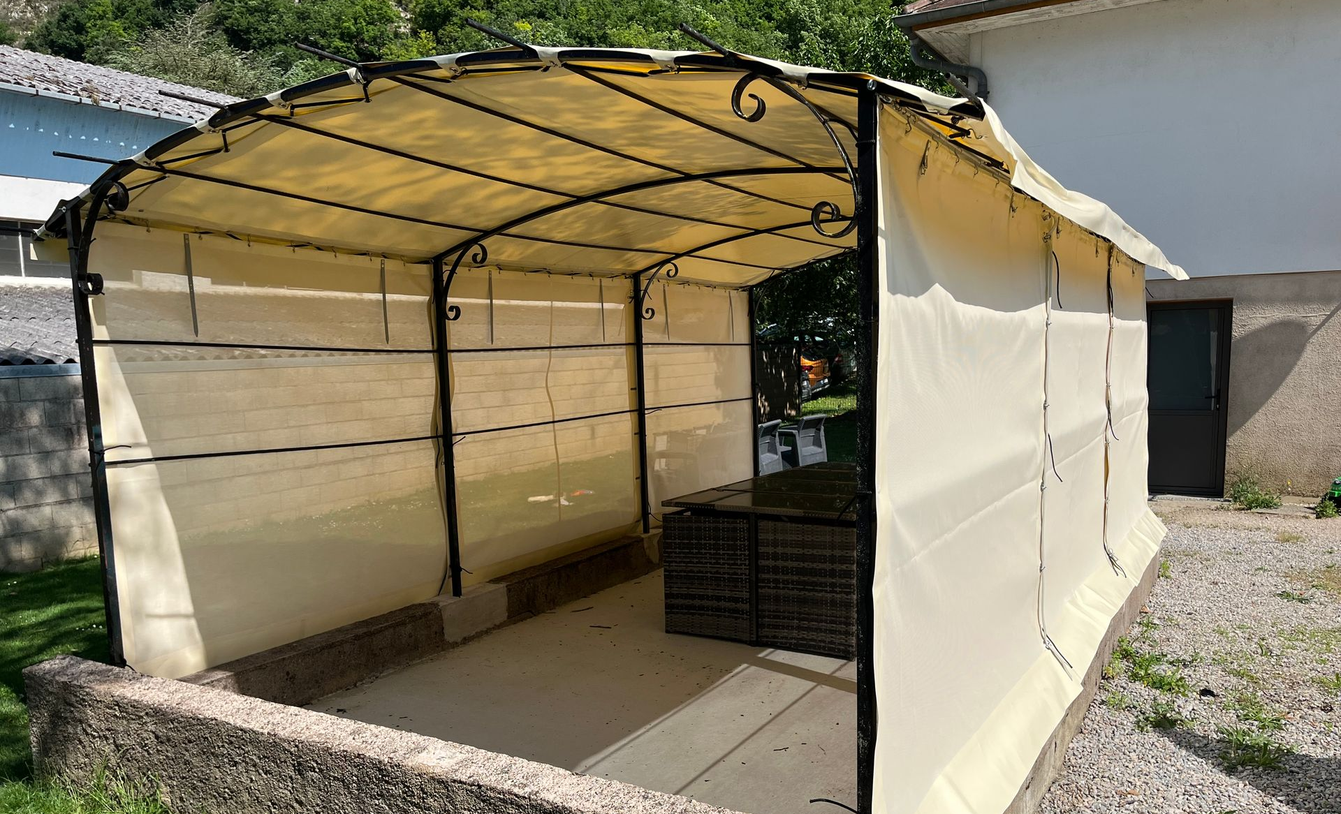 Gazebo beige avec structure et côtés en métal noir, installé sur une terrasse en pierre.