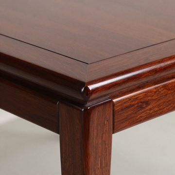 Primer plano de la esquina de una mesa de madera oscura pulida, con borde biselado y pata ahusada