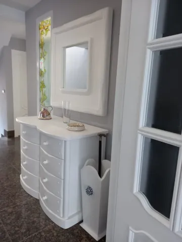 Cómoda blanca con espejo en un pasillo, junto a una ventana y una bandeja decorativa encima