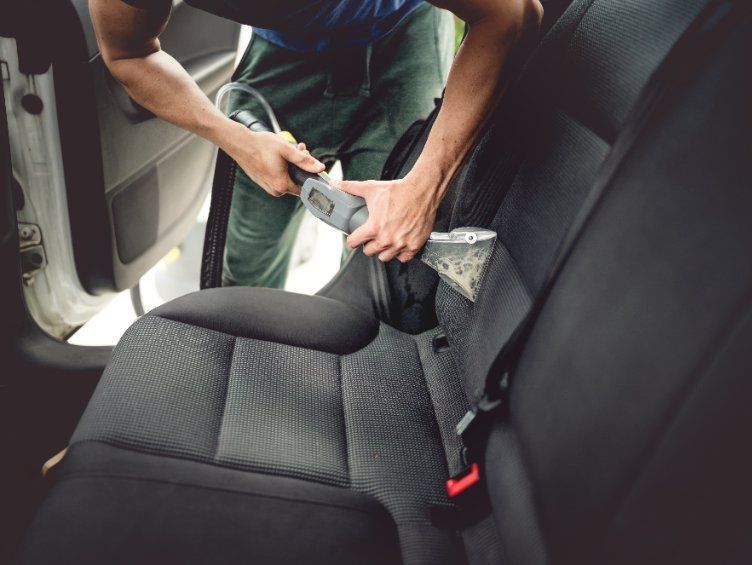 Persona limpiando un asiento de automóvil negro con un limpiador de tapicería de mano.
