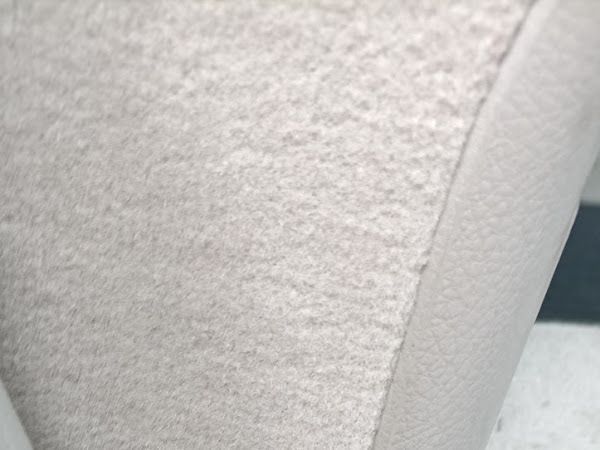 Vista de cerca de una alfombra texturizada de color claro junto a una superficie lisa y ligeramente curva, posiblemente el borde de un mueble.