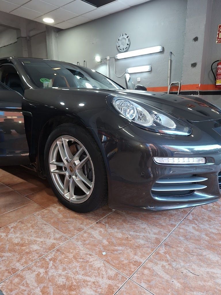 Un Porsche Panamera gris oscuro aparcado en un garaje, con la puerta abierta. El coche tiene llantas plateadas y luces fluorescentes en el techo.