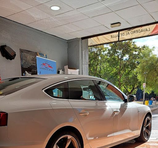 Un coche blanco aparcado en un lavadero. Entra la luz del sol y se ven árboles en el exterior.