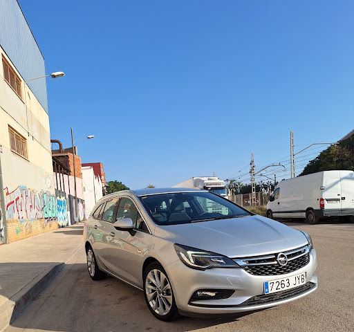 Opel Astra plateado estacionado en una calle con un edificio y un cielo azul claro.