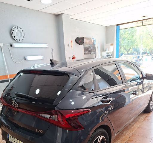 Hyundai i20 hatchback gris oscuro en un taller mecánico, vista trasera. Ventanas tintadas e interior visibles, puerta abierta con vista a la calle.
