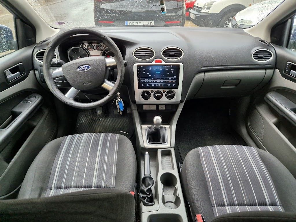 Interior de un Ford Focus; se aprecian los asientos delanteros, el tablero, el volante y una moderna pantalla de infoentretenimiento. Los asientos tienen franjas grises y blancas.