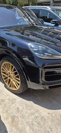 SUV Porsche negro con llantas doradas estacionado sobre una superficie de concreto, la luz del sol reflejándose en el acabado brillante del auto.