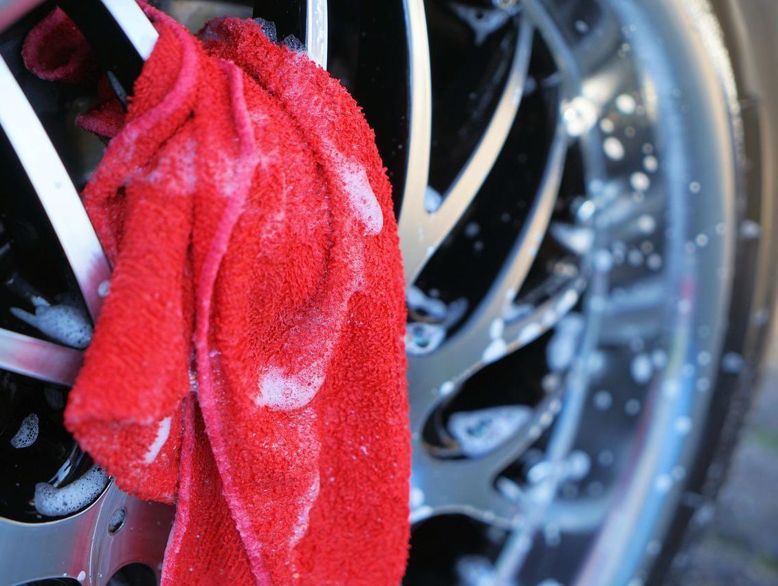 Paño rojo con espuma jabonosa colocado sobre una llanta brillante de un automóvil, probablemente durante la limpieza de una rueda.