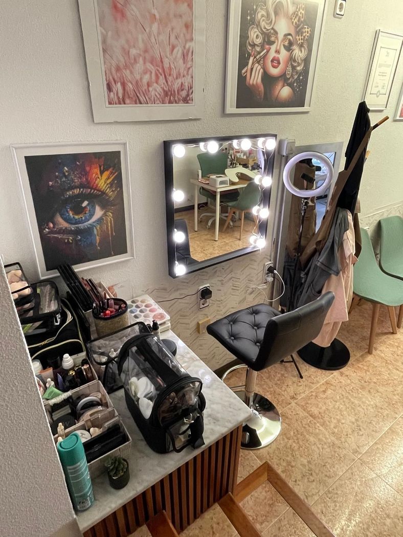 Puesto de peluquería con espejo iluminado, silla, herramientas para el cabello y obras de arte en la pared.