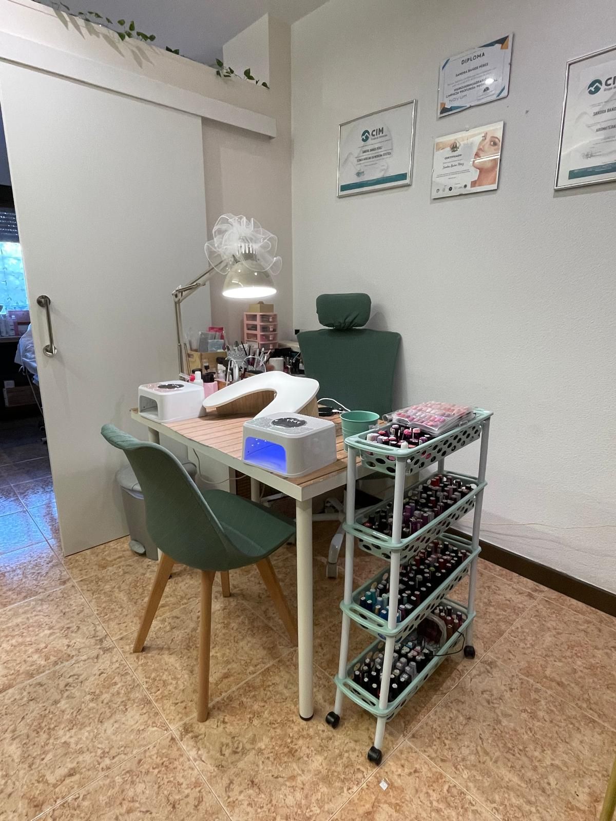 Pequeño puesto de peluquería con silla verde, herramientas de escritorio y estantes con ruedas contra una pared blanca.