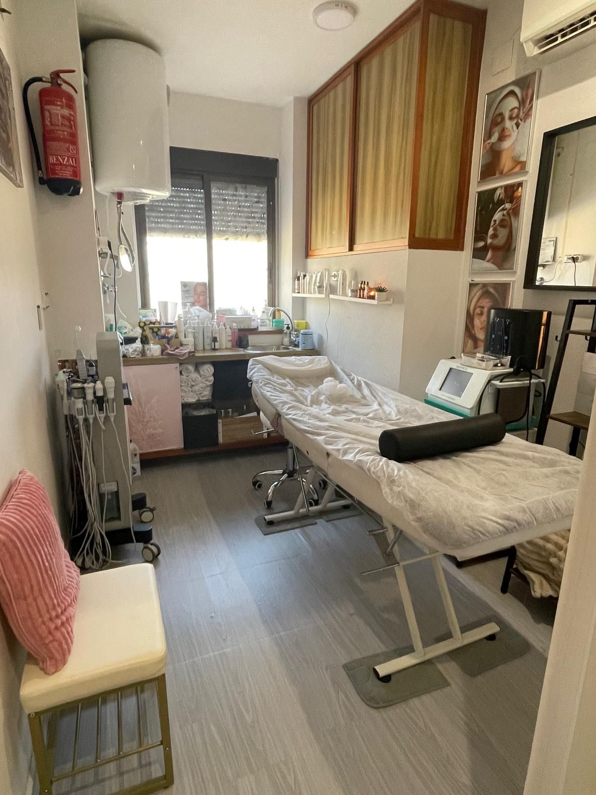 Sala de tratamiento estrecha con camilla de masaje, equipo médico y luz de ventana.