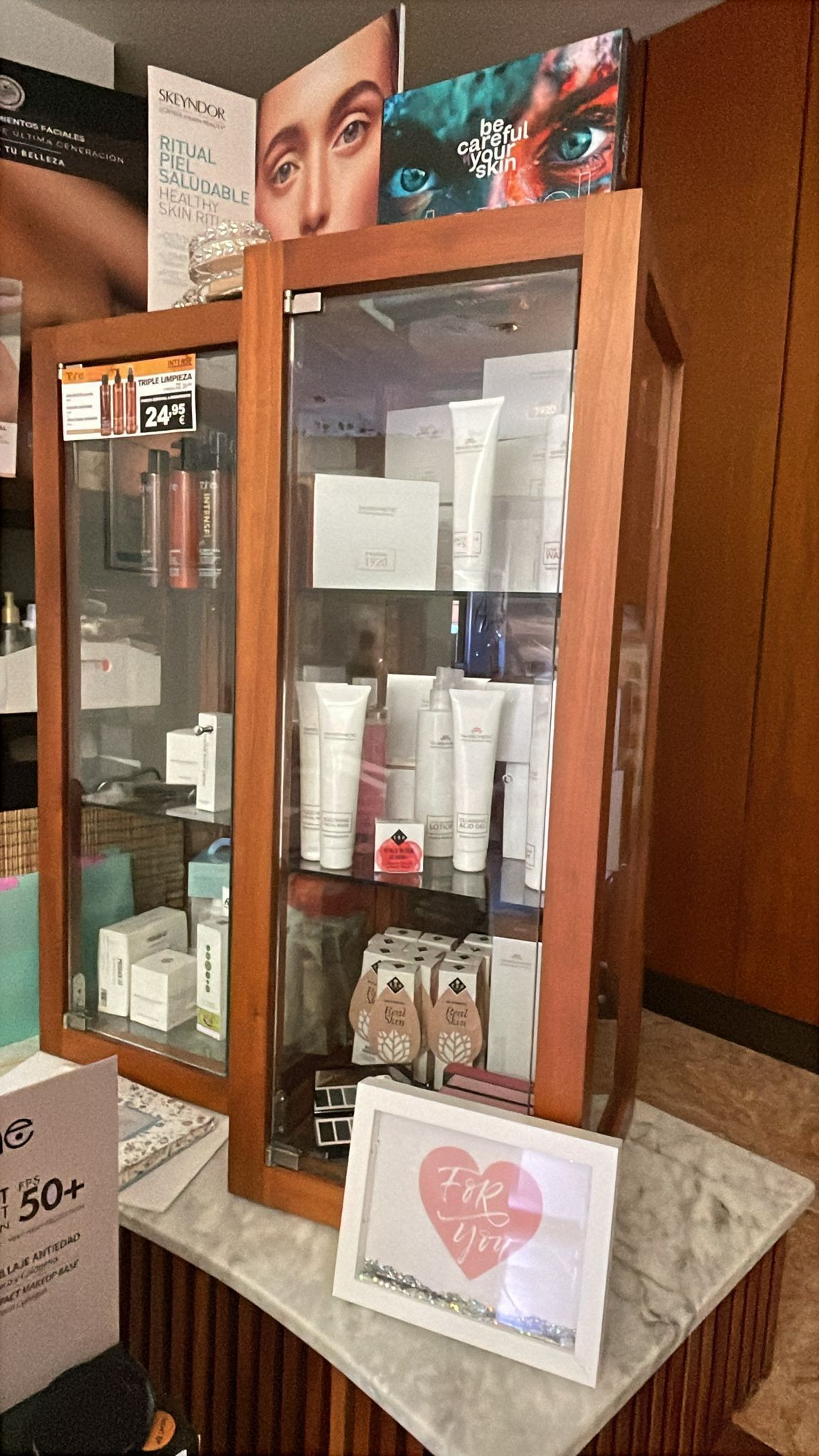 Vitrinas de cristal con productos para el cuidado de la piel y un pequeño cartel rosa con forma de corazón en una tienda.