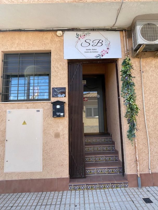 Entrada a la tienda con escaleras, ventana enrejada y pared exterior beige debajo de un letrero blanco.