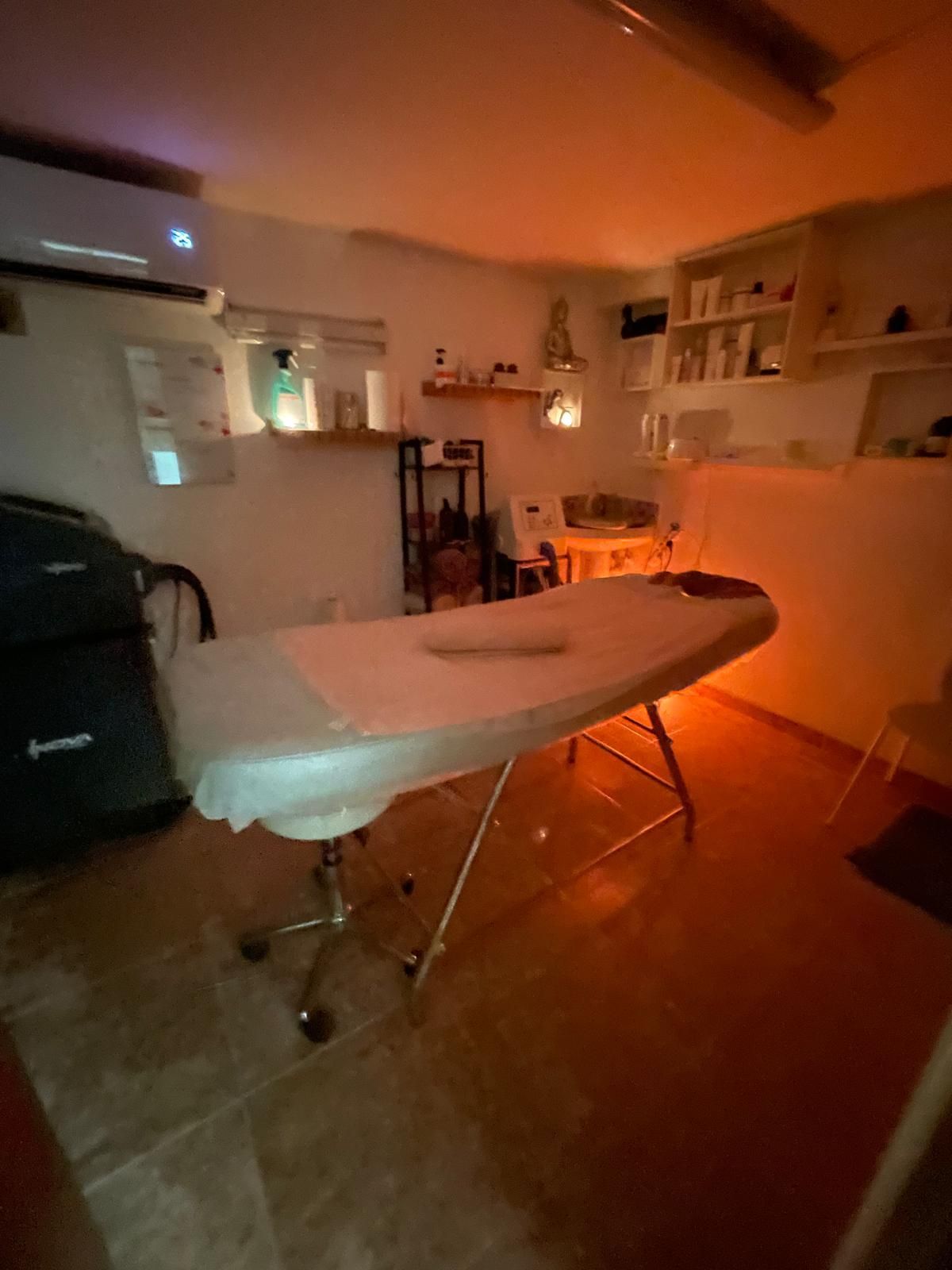 Camilla de masaje en una habitación con poca luz, iluminación cálida de color naranja y estanterías al fondo.