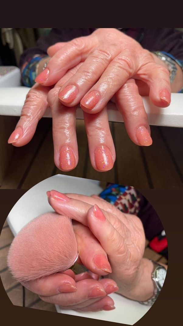 Primer plano de unas manos bien cuidadas con uñas rosas brillantes; una de ellas sostiene una esponja de maquillaje rosa.