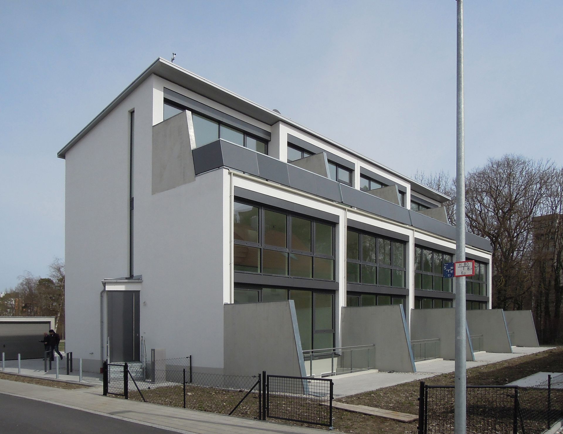 Moderne weiße Stadthäuser mit großen Fenstern und kleinen Balkonen an einem sonnigen Tag.