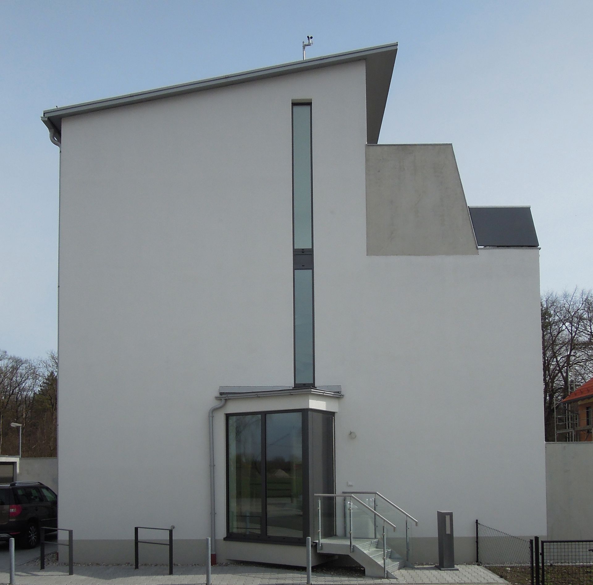 Weißes, modernes Gebäude mit Glaseingang und hohem Fenster unter blauem Himmel.