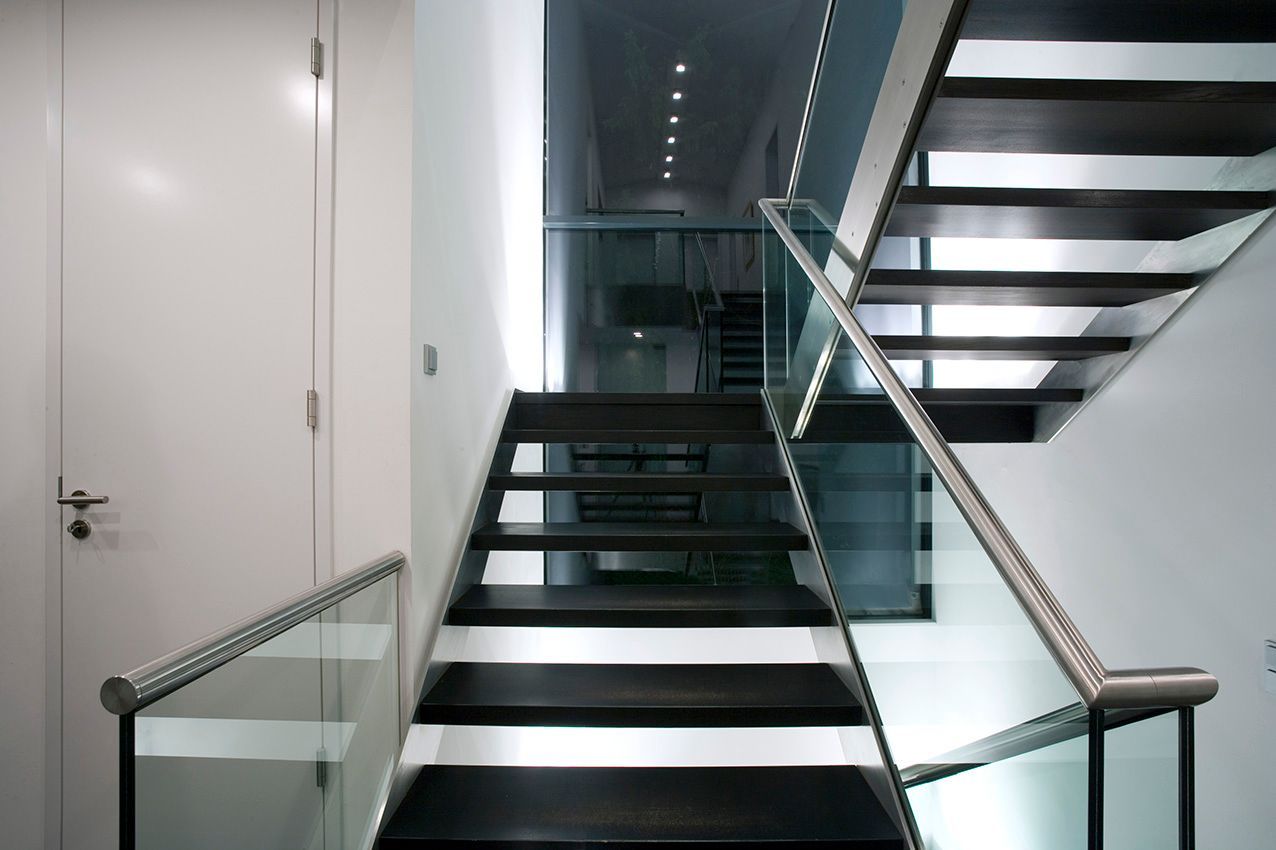 Moderne Treppe mit schwarzen Stufen, Glasgeländer und weißen Wänden.
