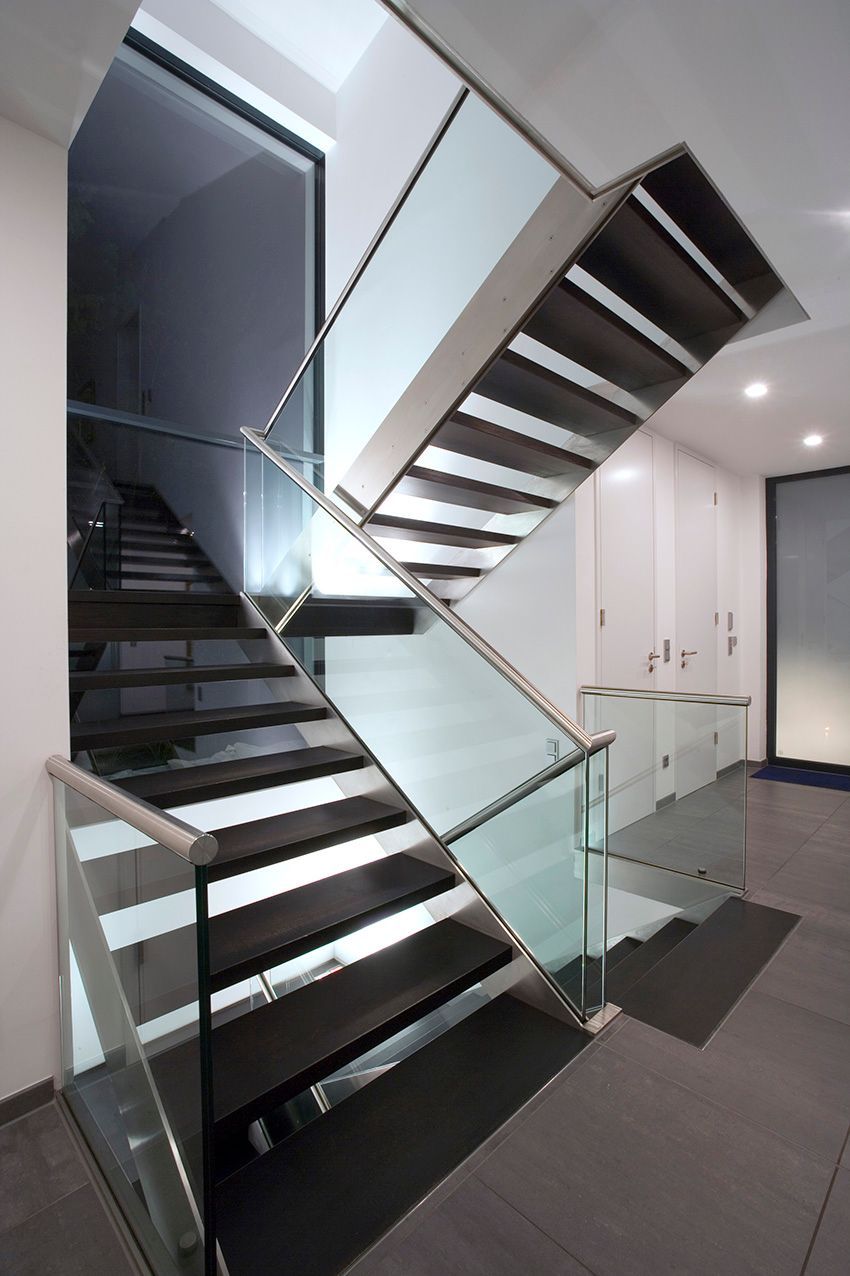 Modernes Interieur mit freitragender Treppe, Glasgeländern und Stufen aus dunklem Holz.