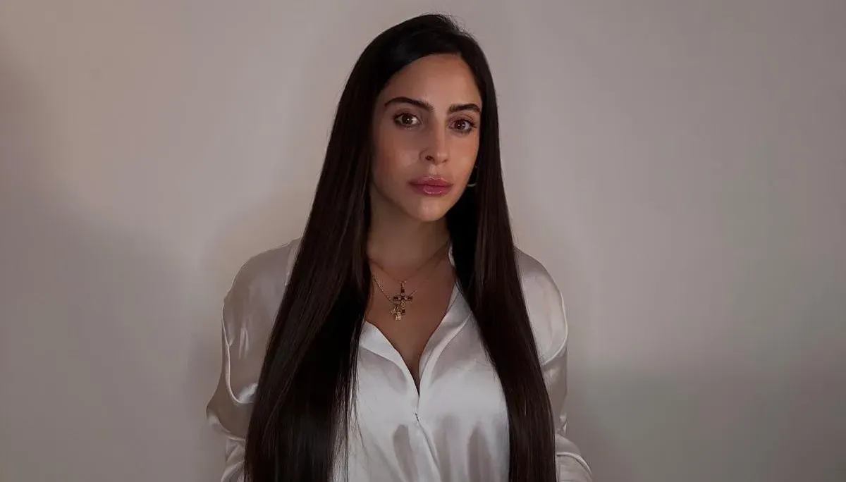 Una persona con cabello largo, liso y oscuro, que viste una blusa