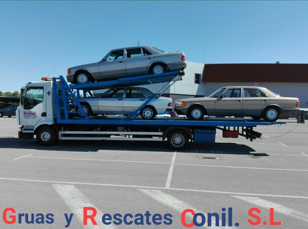 Grúa con tres sedanes en un día soleado. La grúa tiene soporte azul y el nombre 