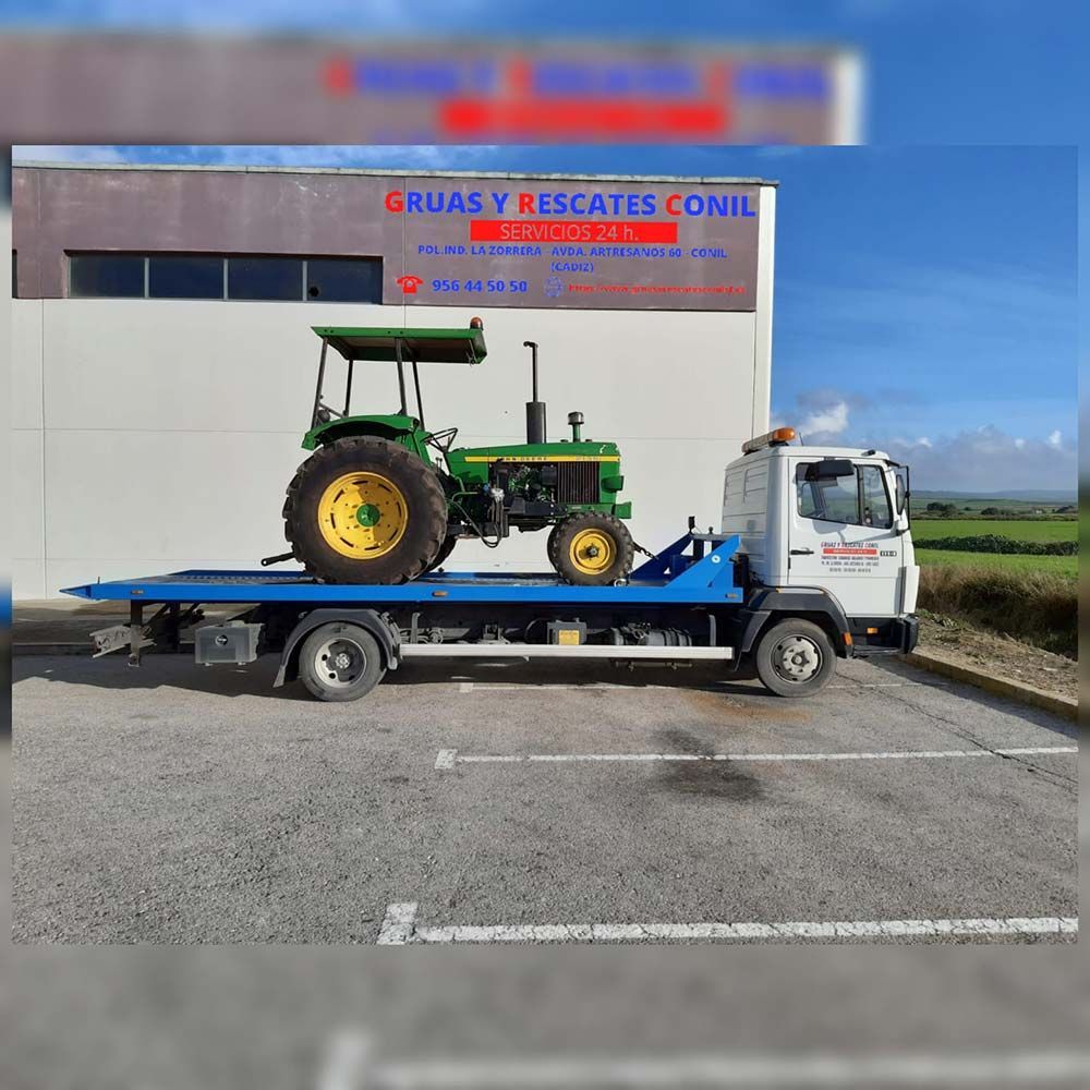 Un tractor John Deere verde siendo transportado en una grúa de plataforma frente a un edificio.