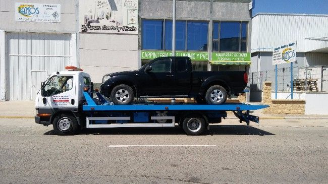 Una camioneta negra sobre una grúa azul en una calle de la ciudad. Edificio al fondo.