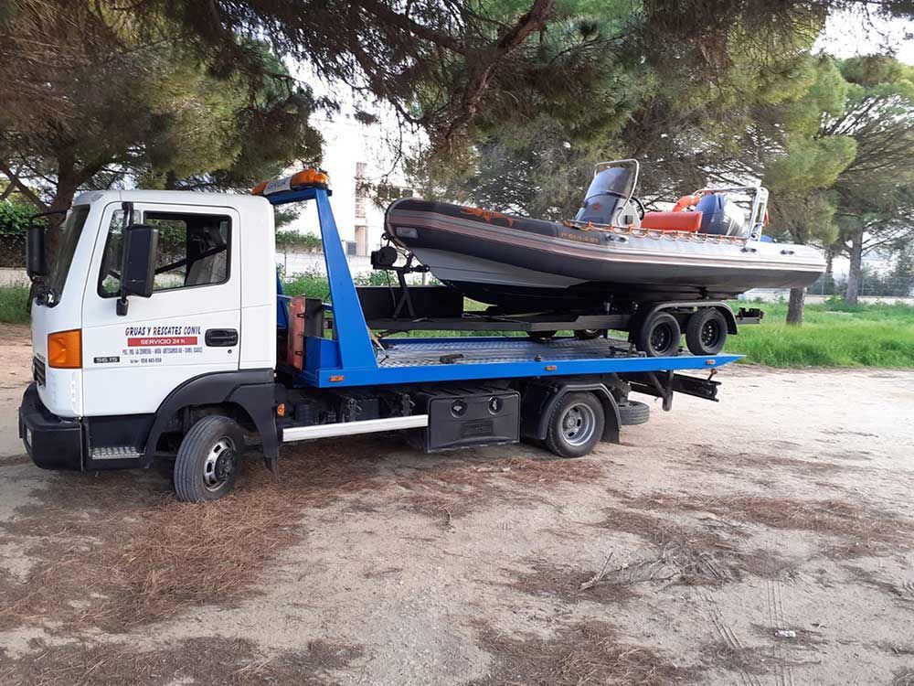 Una grúa transportaba un barco en un remolque, estacionada en un terreno de tierra. La camioneta es blanca y azul.