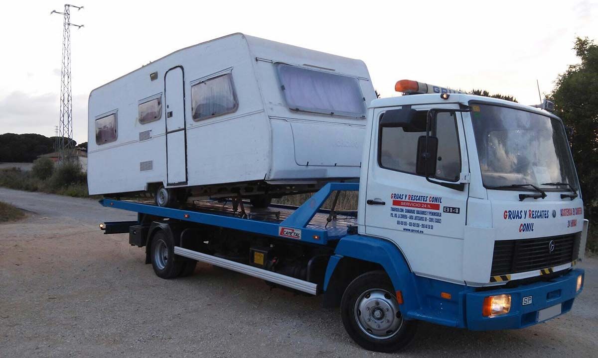 Caravana blanca cargada en una grúa blanca y azul en una carretera.