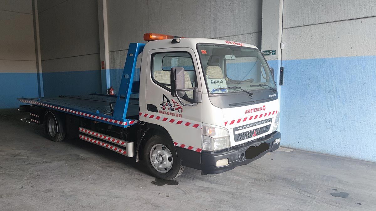 Camión de remolque blanco con pluma azul estacionado dentro de un garaje.
