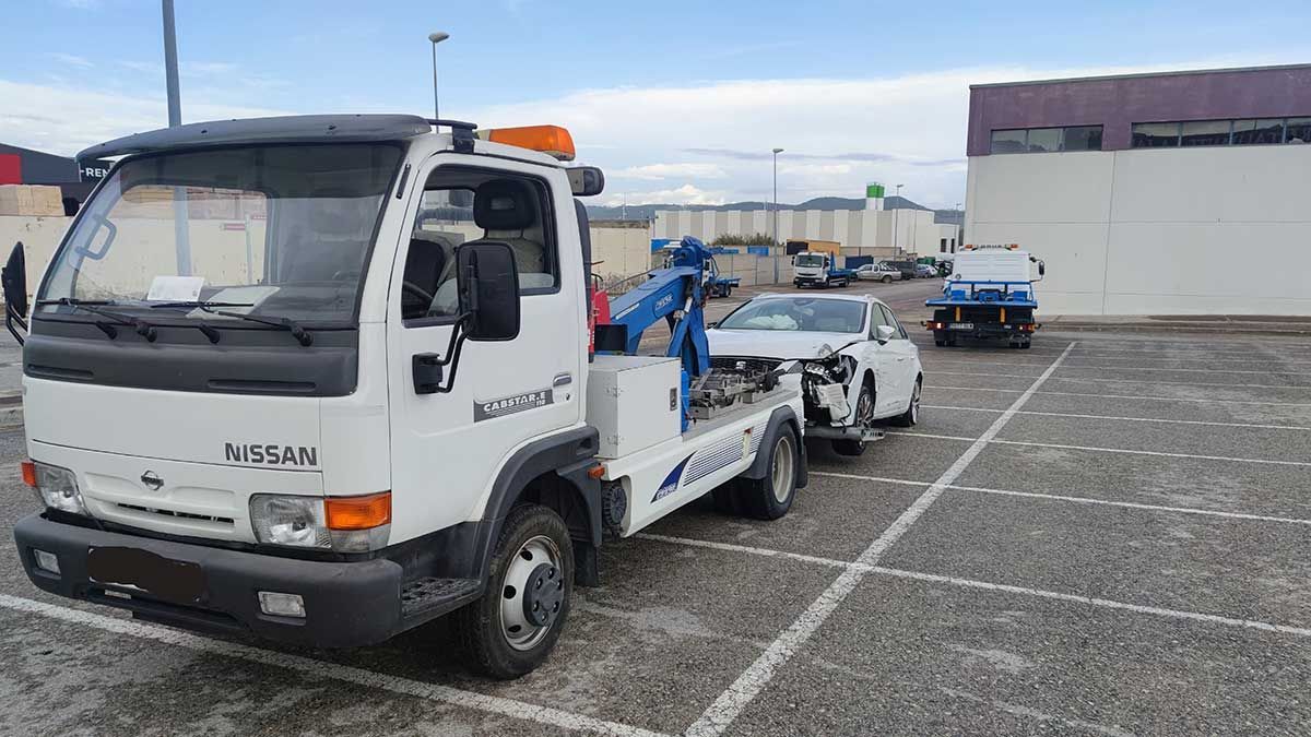 Una grúa blanca transporta un automóvil blanco dañado en un estacionamiento.
