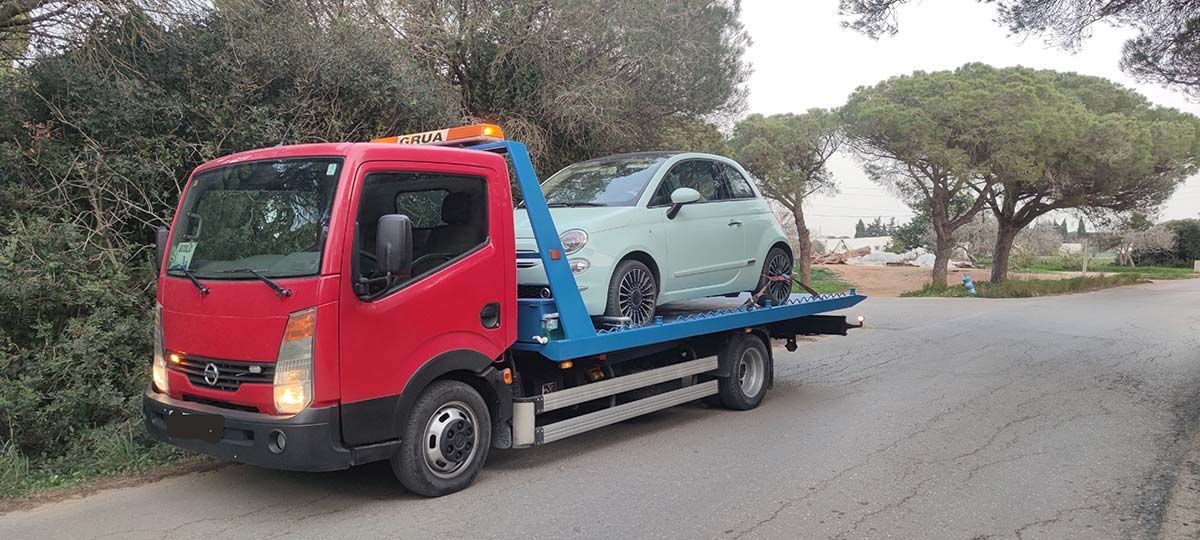 Una grúa roja que transporta un coche verde claro por una carretera.