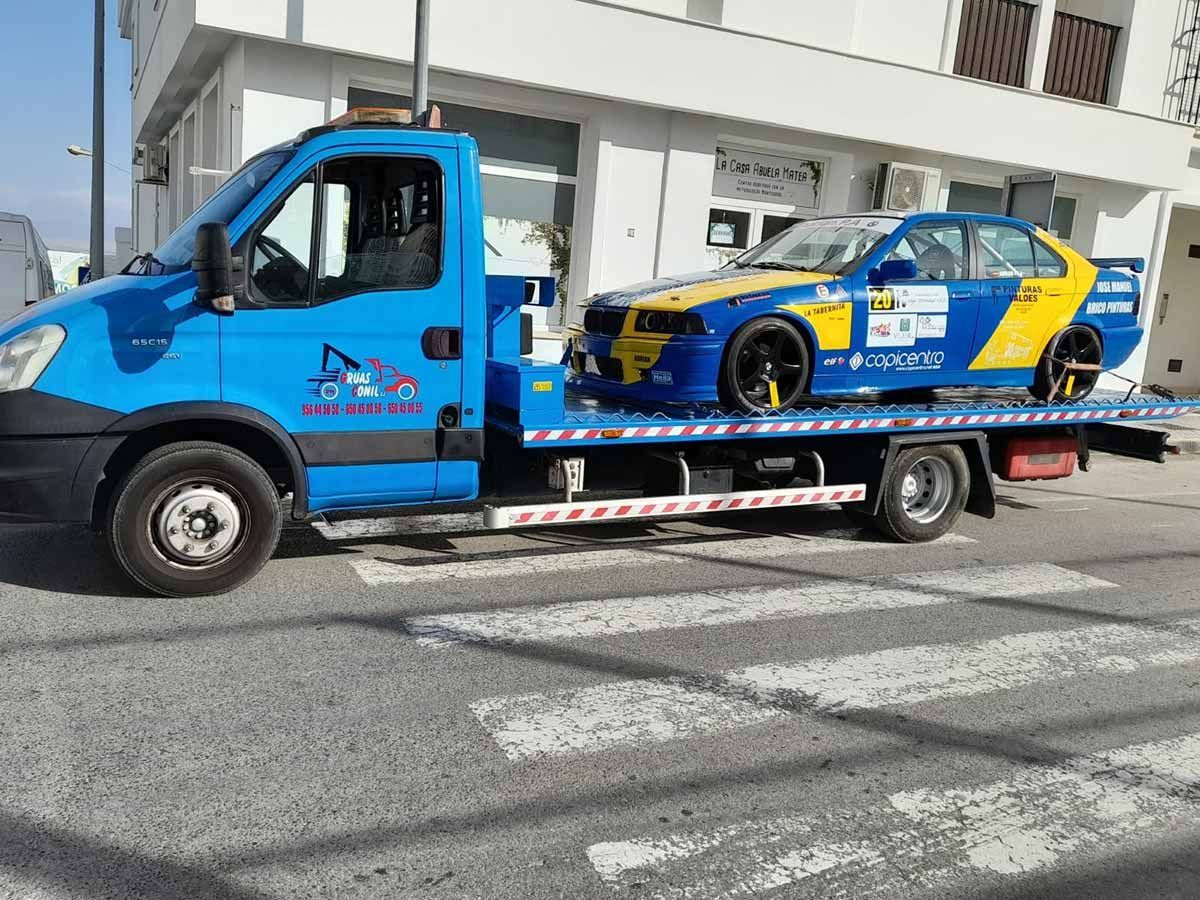 Grúa azul que transporta un coche de carreras azul y amarillo en una calle de la ciudad.