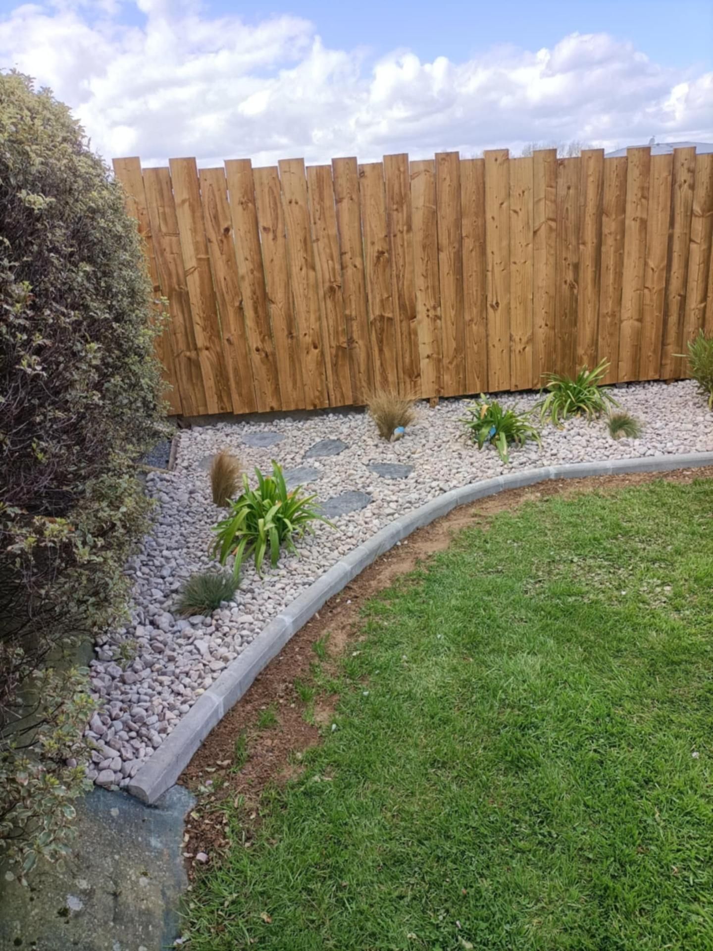 Clôture en bois et parterre de jardin aménagé avec bordure de gazon et de pierres.