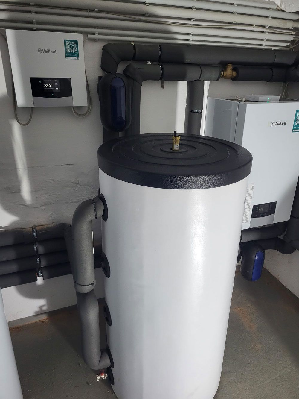 Weißer zylindrischer Wassertank mit schwarzem Deckel und grauen Rohren in einem Hauswirtschaftsraum