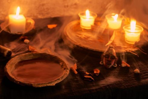 Velas encendidas sobre una mesa oscura con cuencos de barro y una pequeña figurita, un cálido resplandor naranja.
