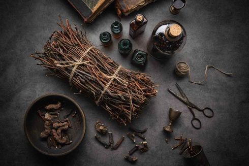 Mesa rústica con hierbas secas, velas, tijeras, botellas y pequeños objetos rituales sobre un fondo oscuro.